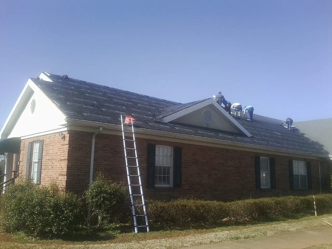 Crew tearing shingles off a brick ranch roof with a ladder set — Metal Roof Repair work by our crew in Pine City