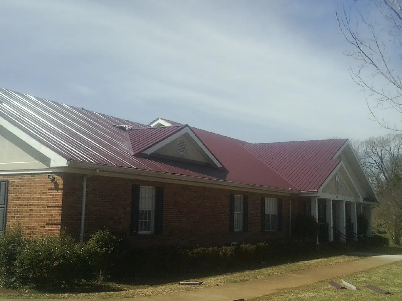 Red metal roof with gabled entries on a long brick building, from a Hail Damage Roof Repair job in Pine City
