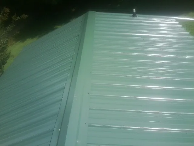 New green metal panels meeting at the ridge of a roof — Flat Roof Repair work by our crew in Pine City