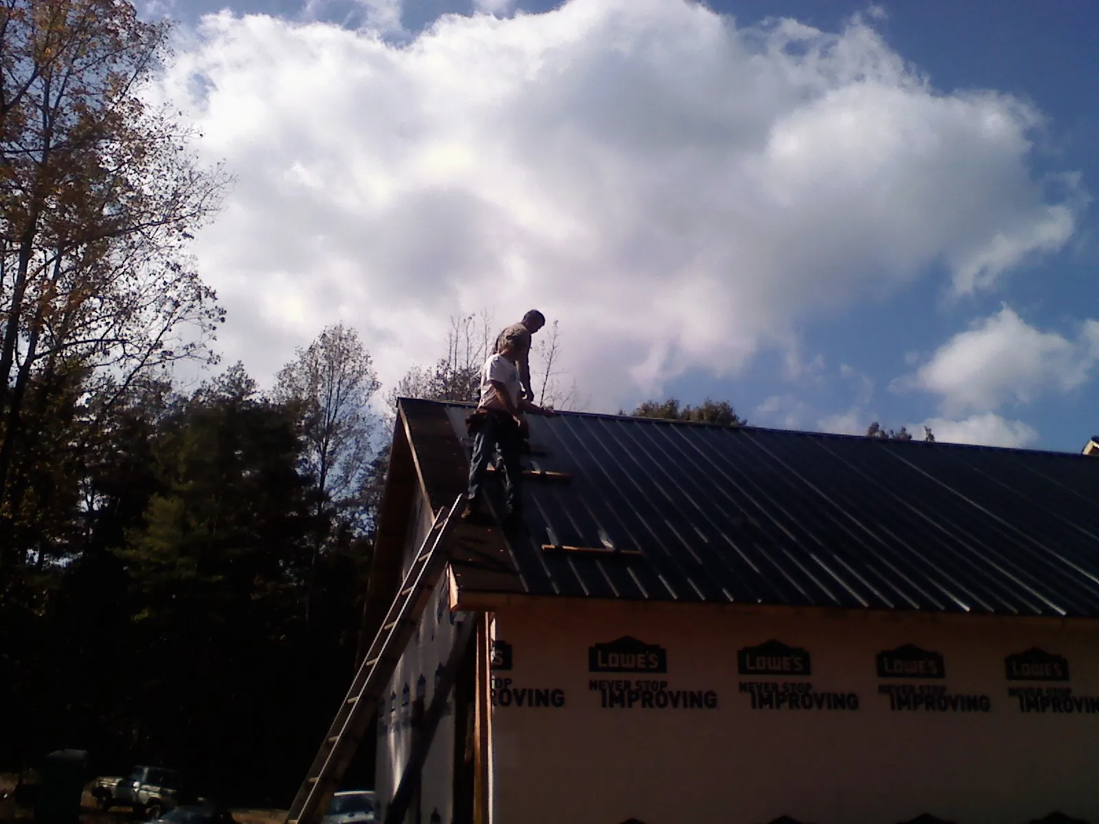 Roofer fastening dark metal panels high against a cloudy sky, from a Roof Inspection job in Pine City