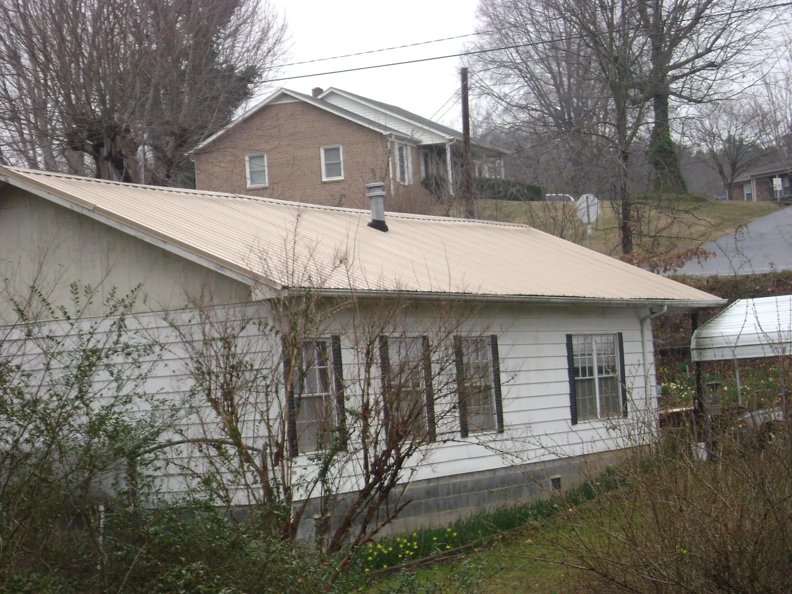 Tan metal roof on a white sided house set into a hillside — Commercial Roofing by Roofing Brothers in Pine City